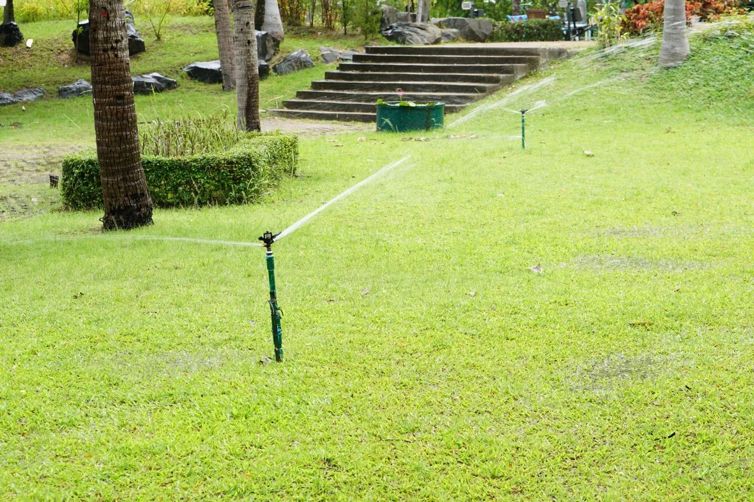 A lawn sprinkler is spraying water on a lush green lawn.