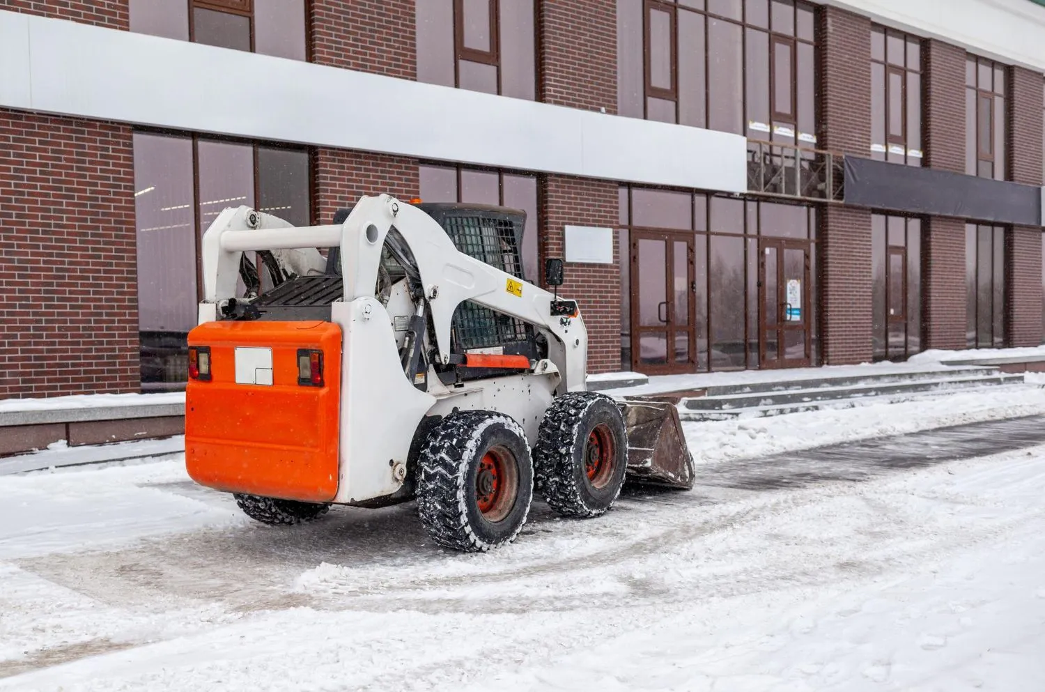 A skid steer is parked in the snow in front of a building.