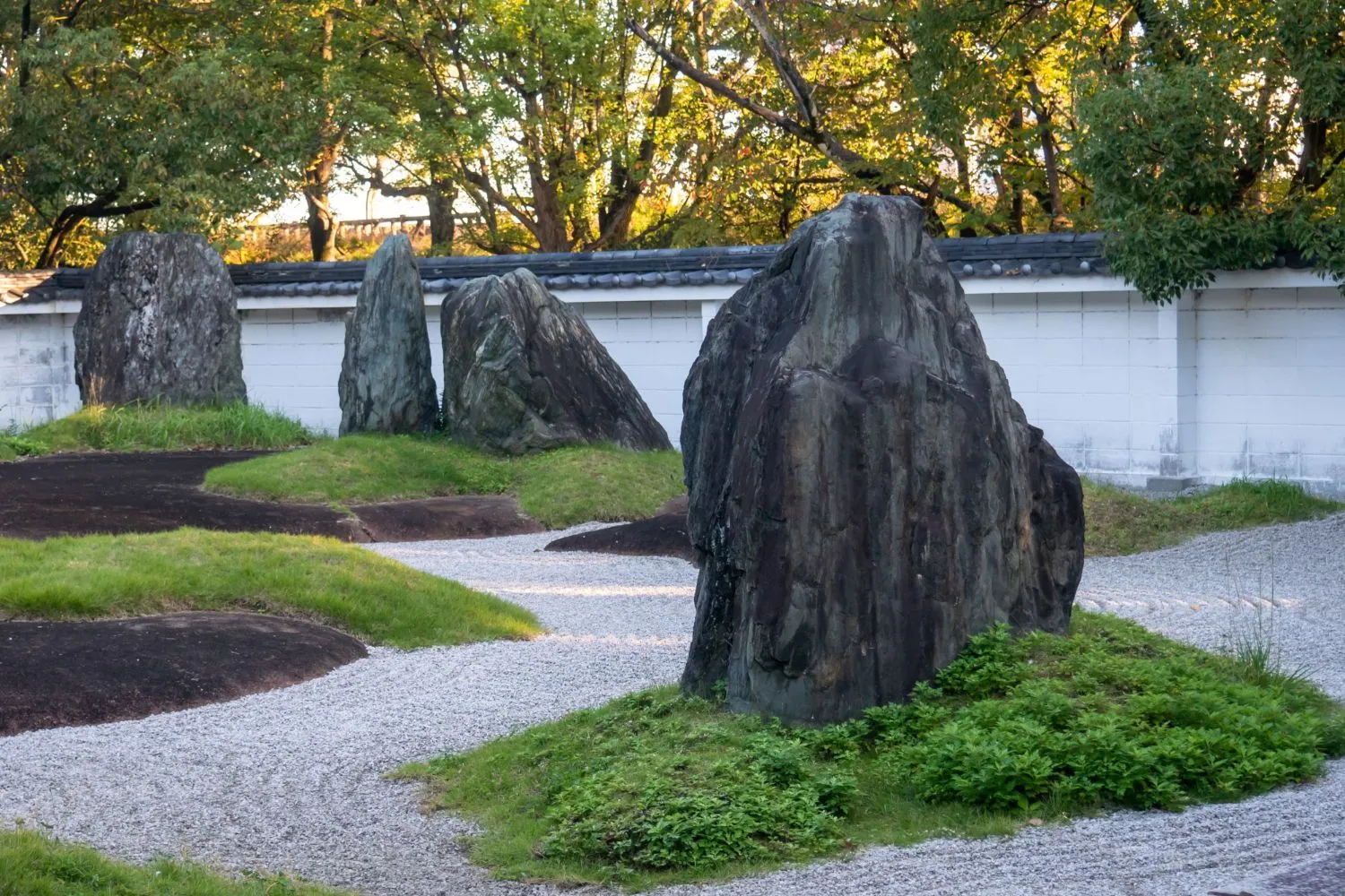 A garden with rocks and grass in front of a white wall.