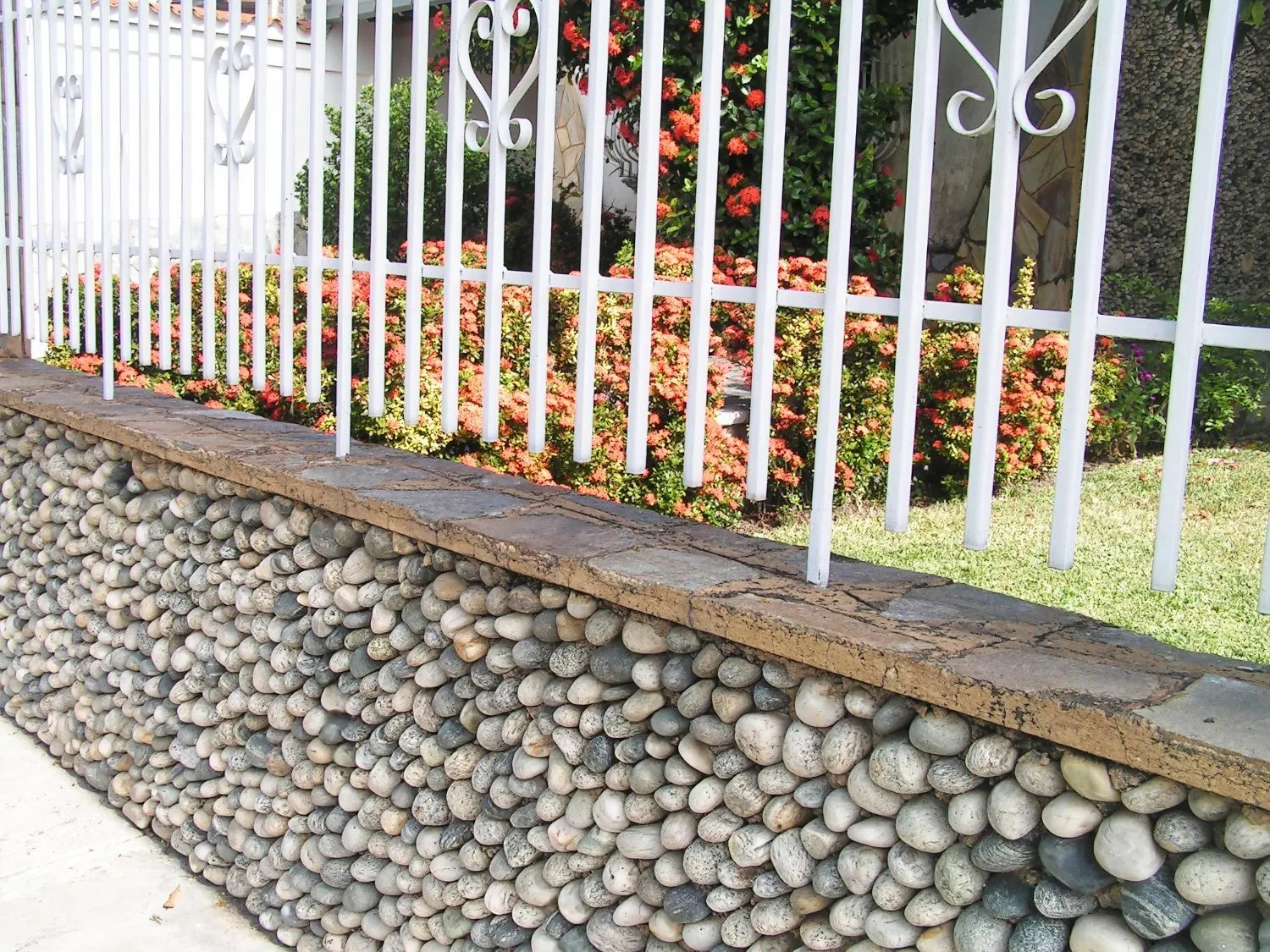 A white fence with a stone wall in front of it
